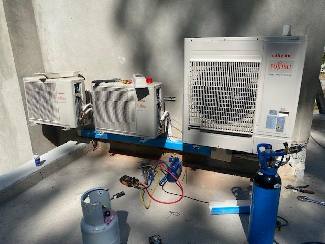 "Trois unités de climatisation Fujitsu montées sur un mur avec des équipements de maintenance, comme un cylindre de gaz bleu et des outils spécialisés.